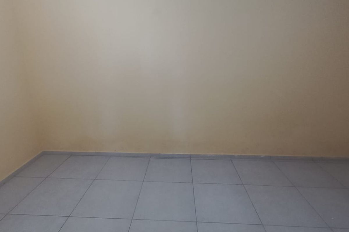 An empty bedroom featuring tiled flooring and neutral walls, showing signs of surface staining near the baseboards.