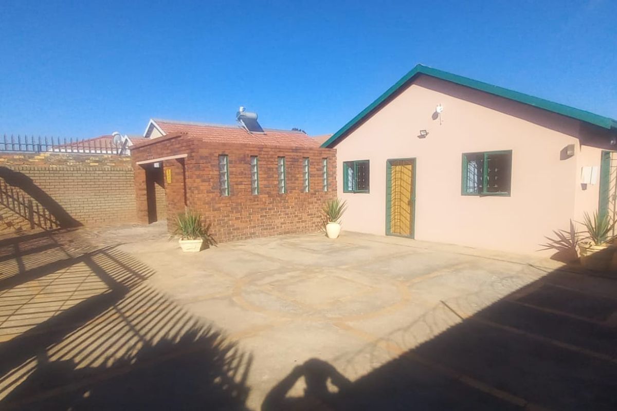 Rear exterior view of the property featuring a paved courtyard, a brick outbuilding with a solar water heater, and secure perimeter fencing.