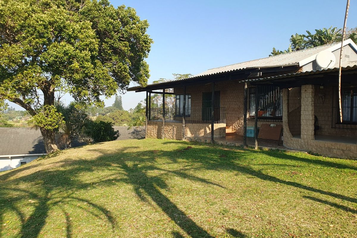 Rear view of the house featuring a covered patio with stone cladding, corrugated roof, and a spacious surrounding garden area.
