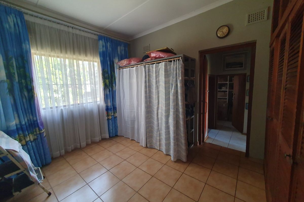 A bedroom featuring tiled flooring and built-in wooden cupboards, with a view into an adjacent hallway.