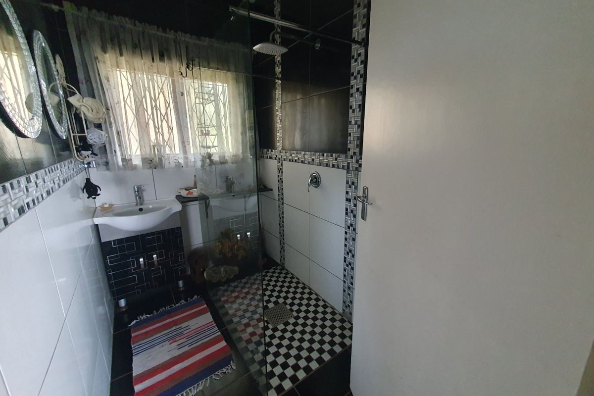 A compact bathroom featuring a glass-enclosed shower with rainfall shower head, wall-mounted basin, and contrasting black and white tiled finishes.