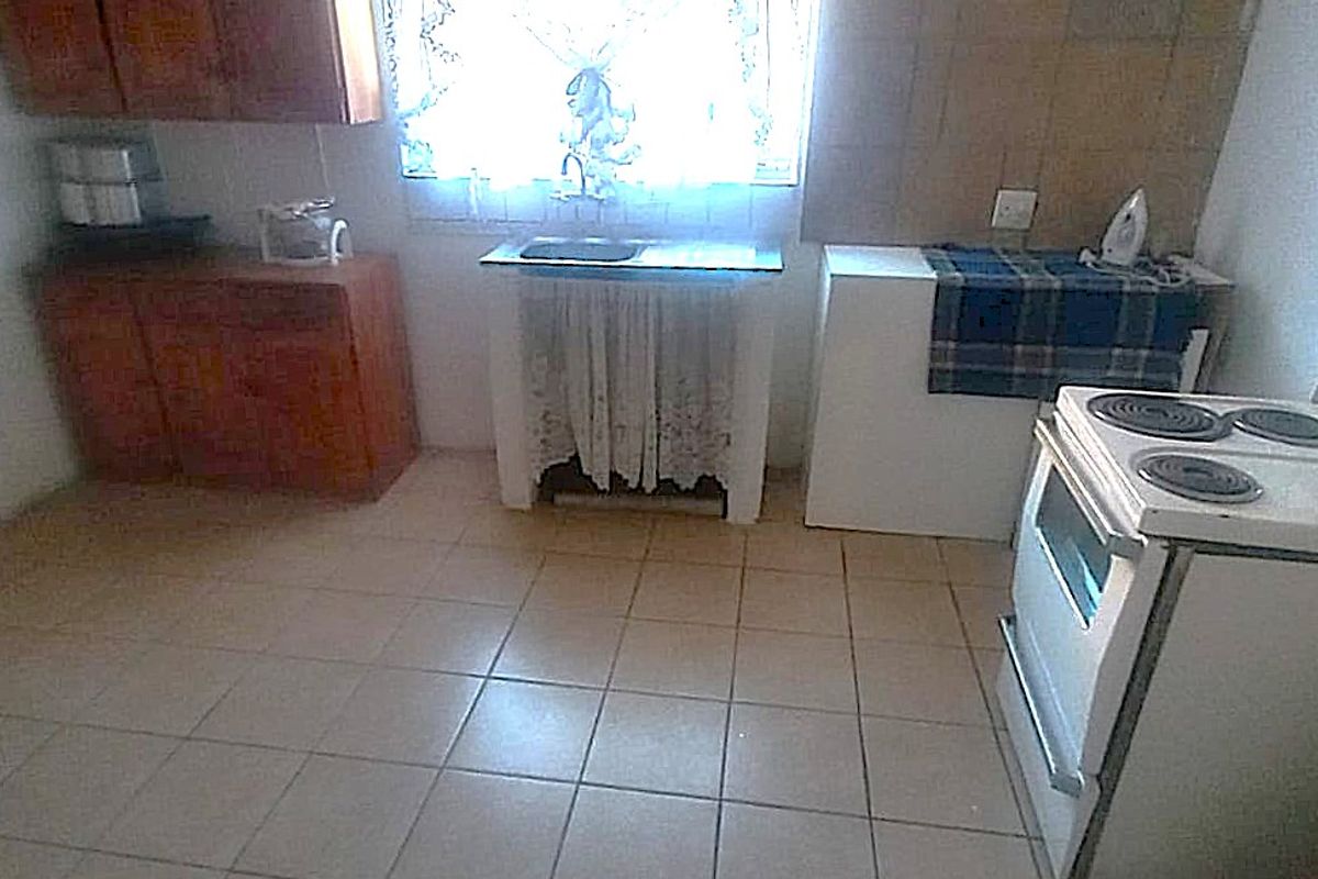 A dated kitchen featuring tiled flooring, built-in wooden cabinetry, a tiled splashback, and a freestanding electric stove.
