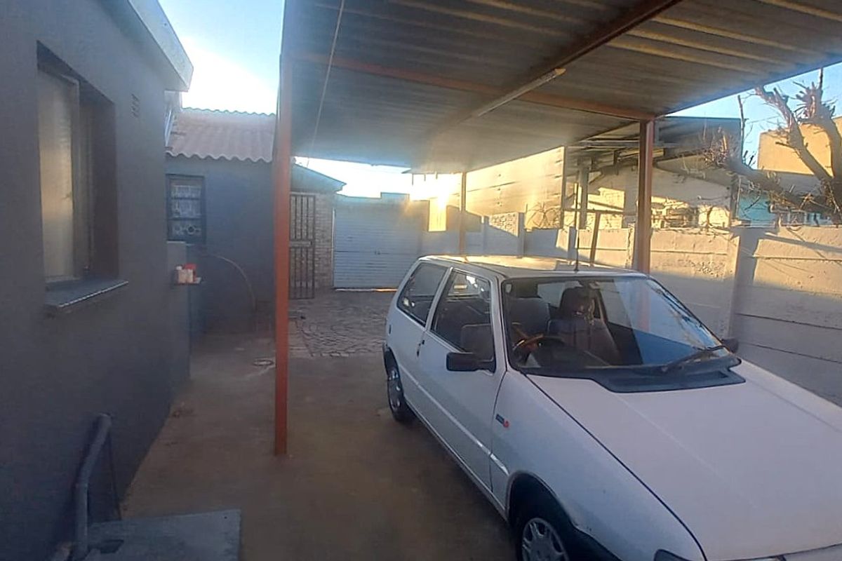 Rear exterior area featuring a covered carport structure, paved driveway, and perimeter boundary walling.
