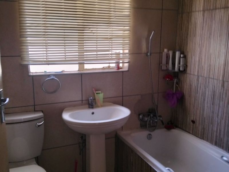 A functional bathroom featuring a pedestal basin, bathtub with shower mixer, and tiled finishes throughout.