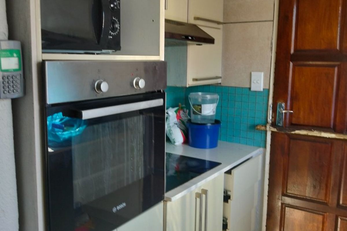 Compact kitchen featuring built-in oven, hob, extractor fan, and tiled backsplash, with direct access to an exterior timber door.