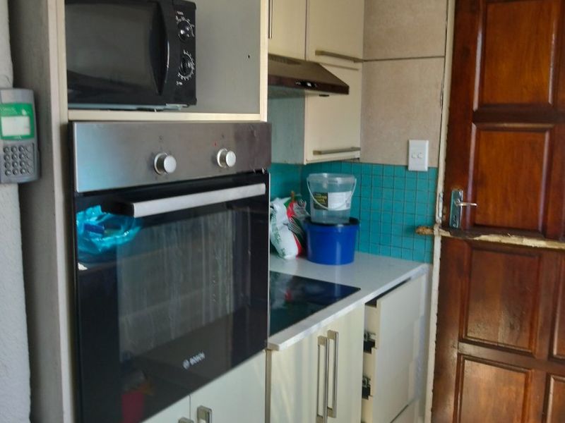 Compact kitchen featuring built-in oven, hob, extractor fan, and tiled backsplash, with direct access to an exterior timber door.
