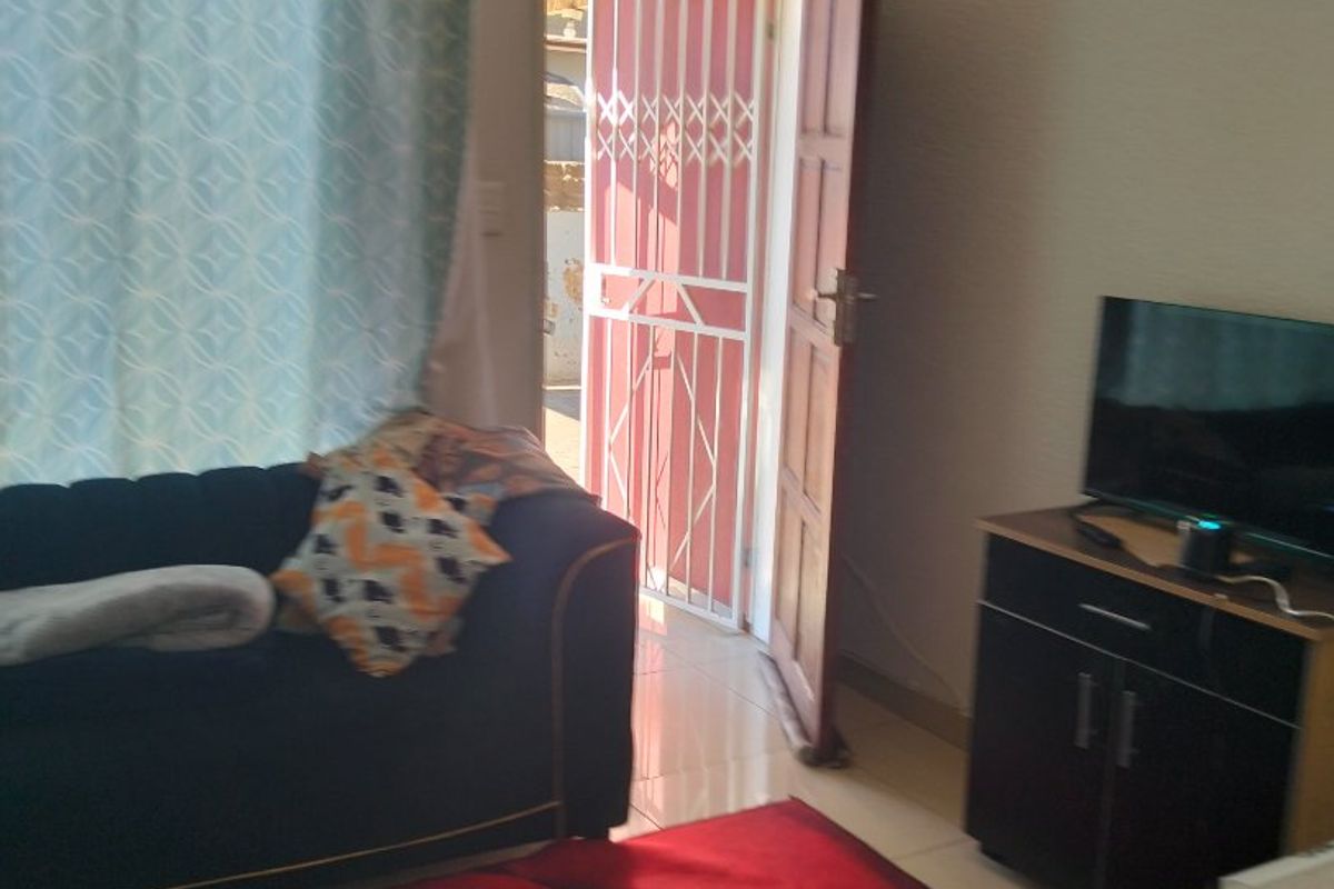A living room area featuring tiled flooring and a security gate at the entrance door, providing access to the exterior.