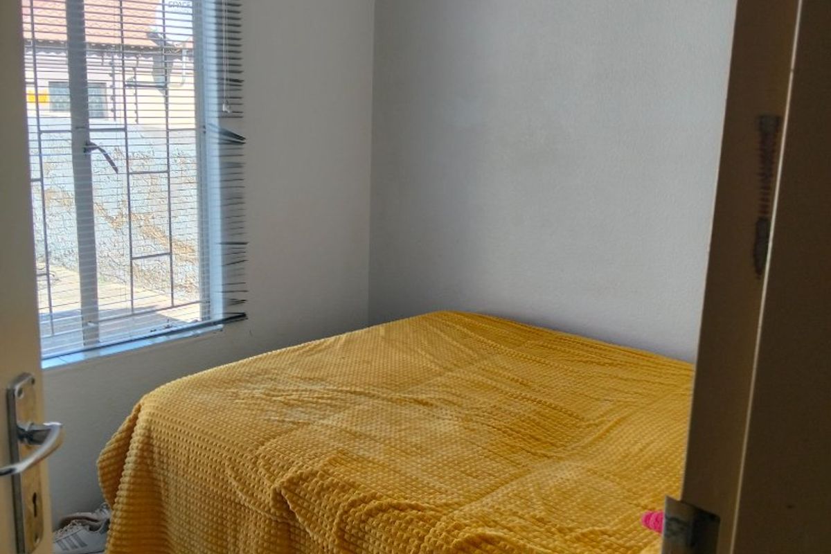 A compact bedroom featuring neutral walls and a window fitted with venetian blinds, offering a functional space for rest.