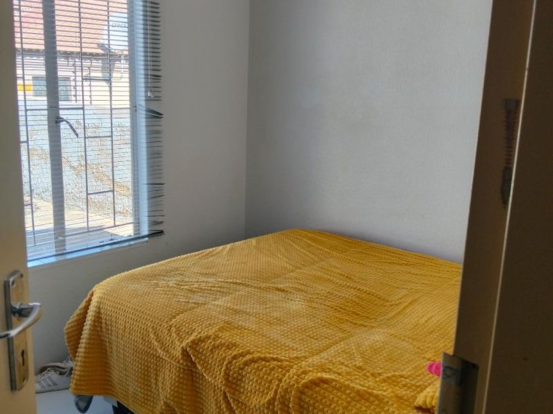 A compact bedroom featuring neutral walls and a window fitted with venetian blinds, offering a functional space for rest.