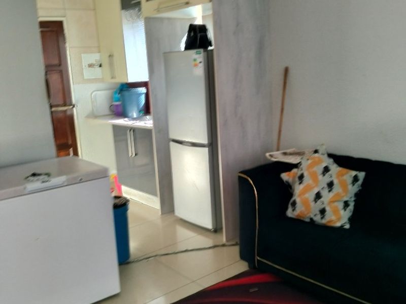 An open-plan living area featuring a compact kitchen with built-in cabinetry and tiled flooring throughout.