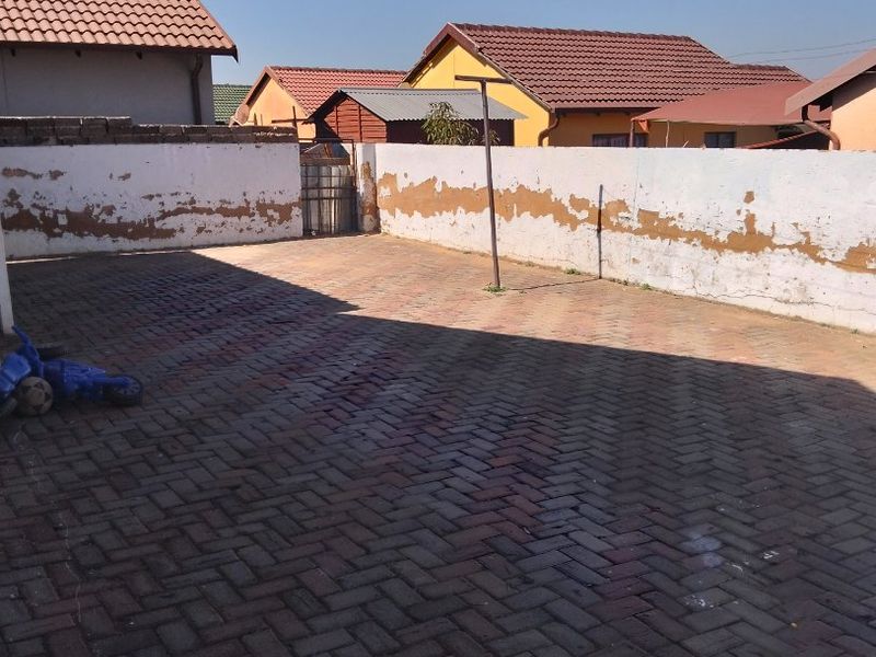 A paved rear courtyard area enclosed by boundary walls, featuring a metal gate and requiring maintenance to the wall finishes.