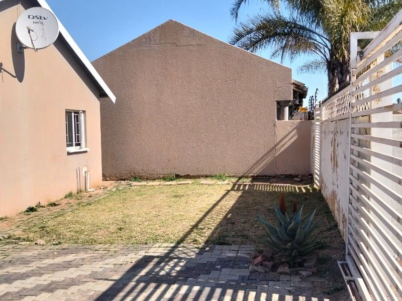 A rear exterior view showing a paved area, a small lawn, and a boundary wall with visible wear and peeling paint.