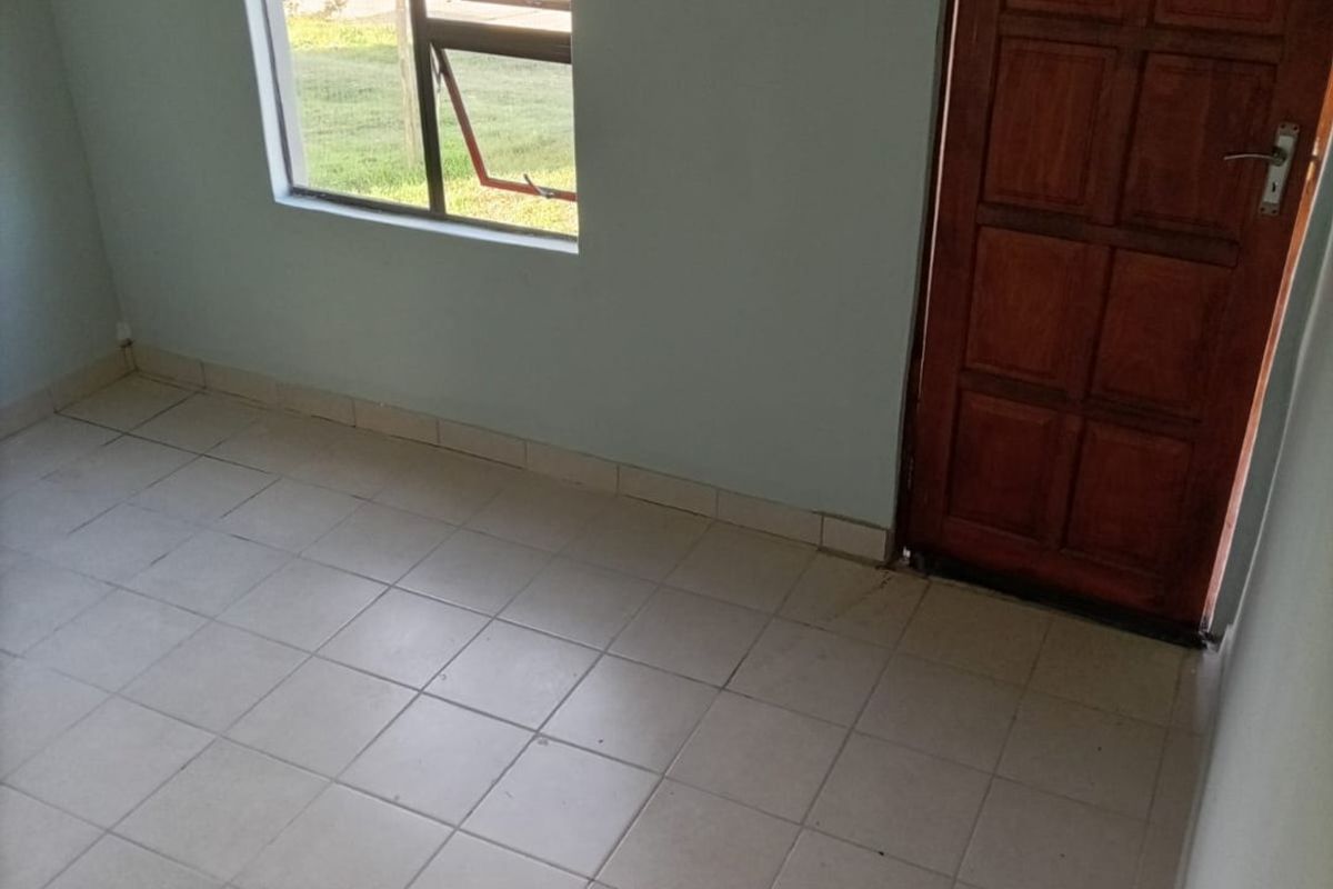 An empty bedroom featuring tiled flooring, a timber door, and a casement window, providing a blank canvas for potential interior design updates.