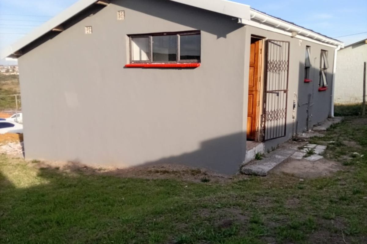 A view of the rear exterior of the house featuring a grey rendered facade, security gate, and basic window installations.