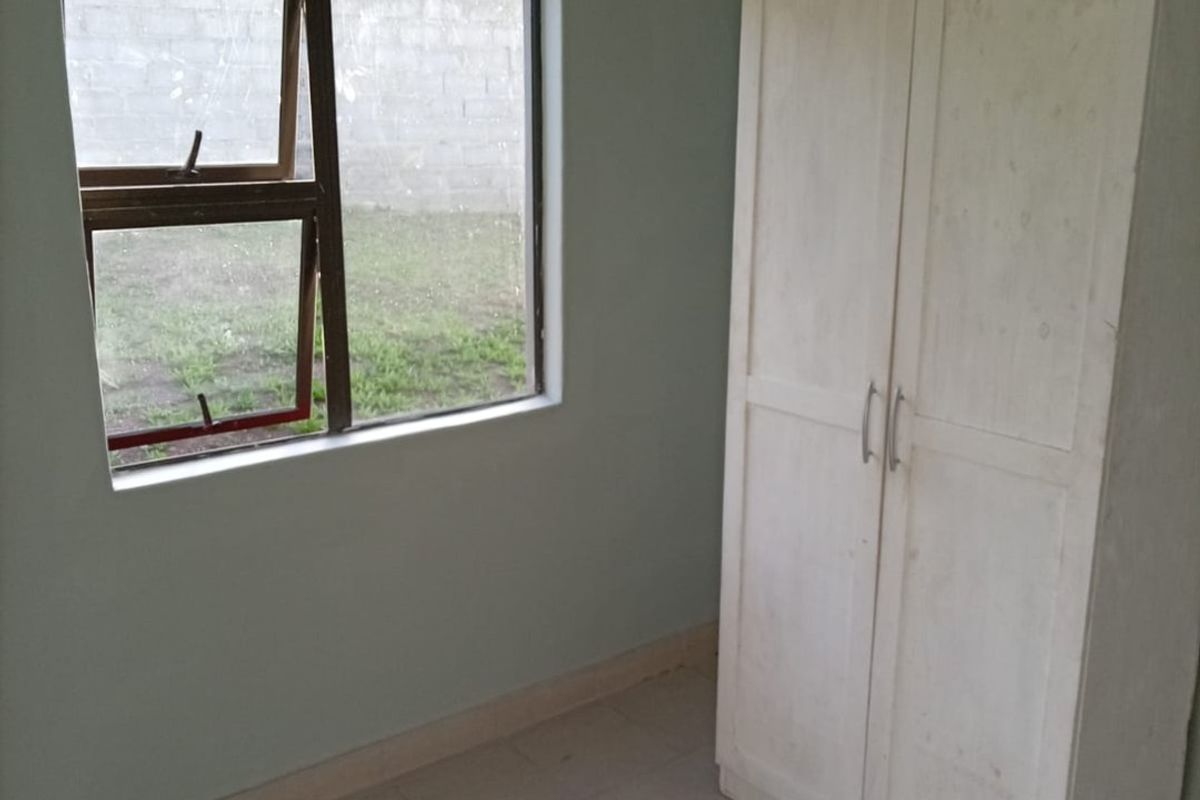 A simple bedroom featuring tiled flooring, a built-in wardrobe, and a window overlooking the rear yard.