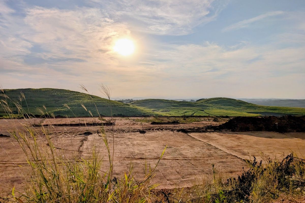A wide-angle view of a cleared, graded residential plot of land with rolling green hills in the background.