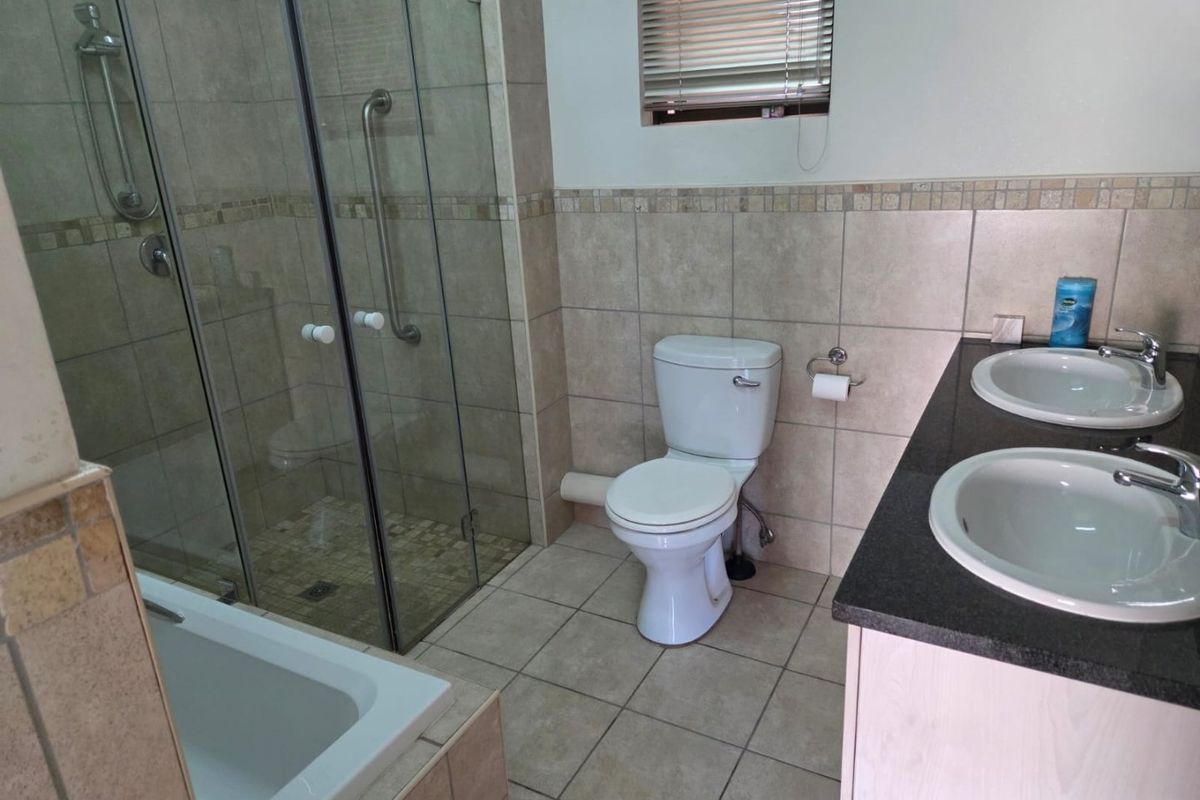A clean, functional bathroom featuring a double vanity with granite countertops, a glass-enclosed shower, and a built-in bathtub with neutral tile finishes.