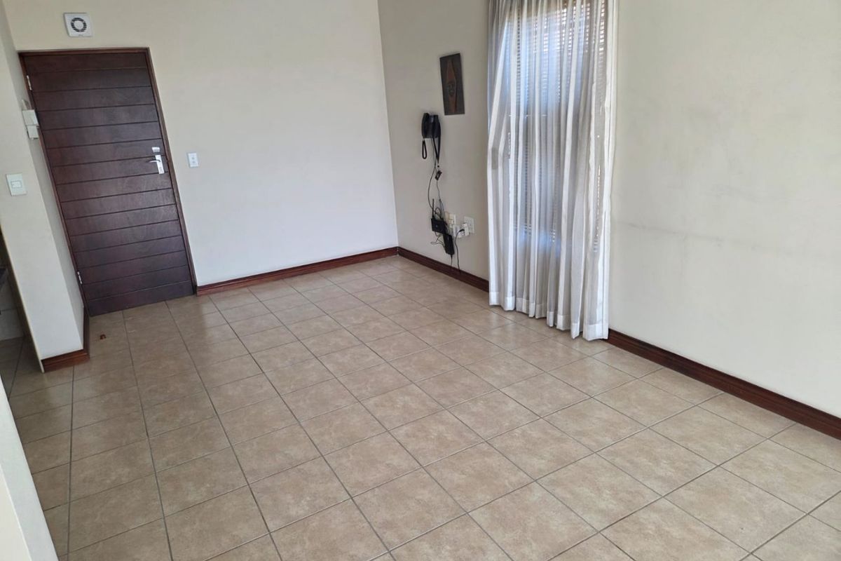 An empty living room featuring neutral tiled flooring, a dark timber door, and wall-mounted electrical points.