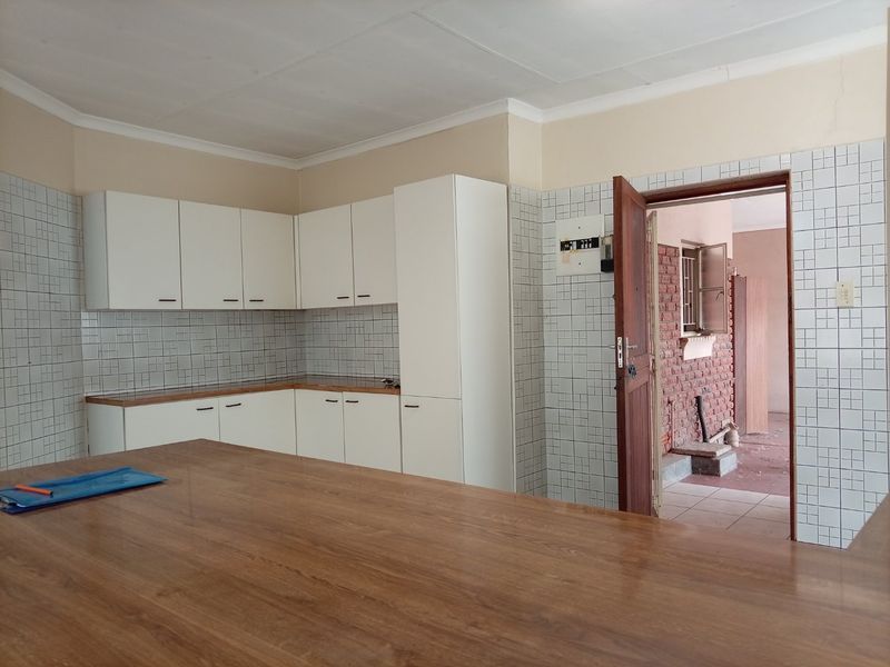 A functional kitchen featuring white built-in cabinetry, tiled splashbacks, and a wooden countertop, with an adjacent doorway leading to an exterior area.