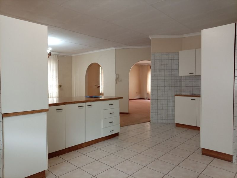 Open-plan kitchen area featuring tiled flooring, built-in cabinetry, and archway transitions leading to adjacent living spaces in a dated apartment interior.
