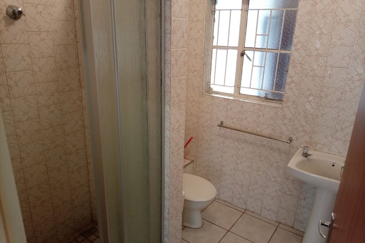 A functional bathroom featuring a shower enclosure, pedestal basin, and toilet, finished with dated wall tiles and tiled flooring.
