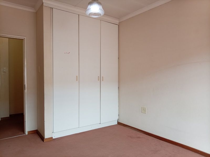 An empty bedroom featuring built-in wardrobes, carpeted flooring, and neutral wall finishes, offering a blank canvas for potential updates.