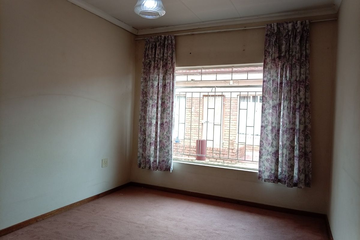 An empty bedroom featuring carpet flooring, security bars on the window, and a ceiling light fixture, ready for renovation or staging.