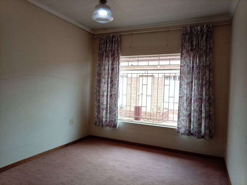 An empty bedroom featuring carpet flooring, security bars on the window, and a ceiling light fixture, ready for renovation or staging.