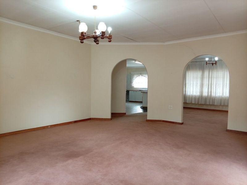 Spacious, empty living area featuring arched doorways leading to adjacent rooms, carpeted flooring, and traditional ceiling light fixtures.