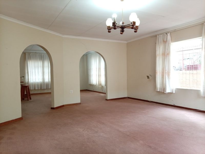 Spacious, empty living area featuring distinctive architectural archways, carpeted flooring, and natural light through windows fitted with security bars.