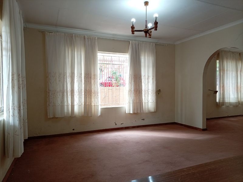 An empty living room featuring an arched entryway, carpeted flooring, and security bars on the windows, requiring cosmetic updates to the walls and flooring.