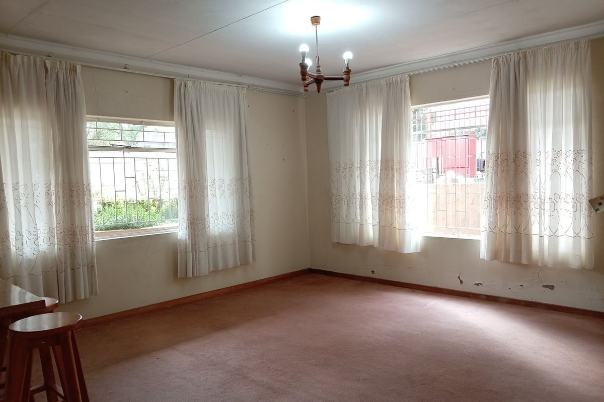 Spacious living area featuring large windows with security bars, carpeted flooring, and neutral walls, offering a blank canvas for renovation.