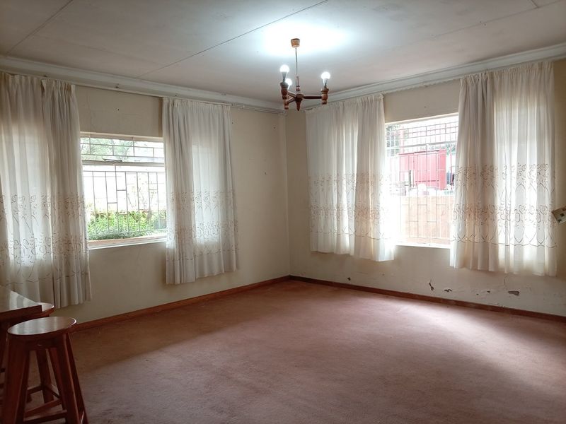 Spacious living area featuring large windows with security bars, carpeted flooring, and neutral walls, offering a blank canvas for renovation.