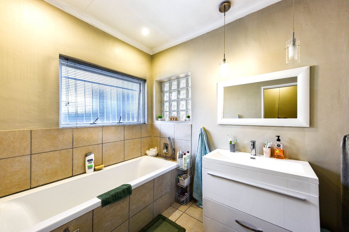 A well-maintained bathroom featuring a built-in bathtub with tiled surround, a modern vanity unit with basin, and a combination of glass block and standard windows.