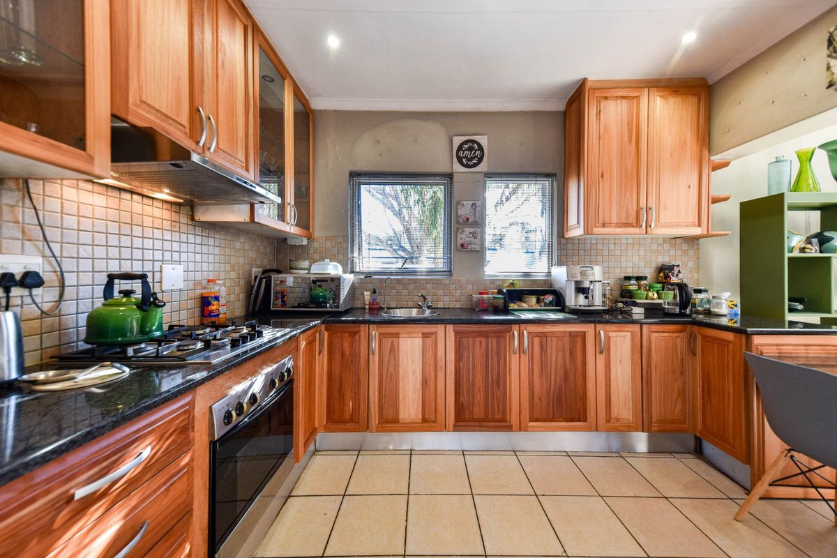 A functional kitchen featuring warm-toned wooden cabinetry, granite countertops, a gas hob with extractor, and tiled flooring with a classic backsplash.