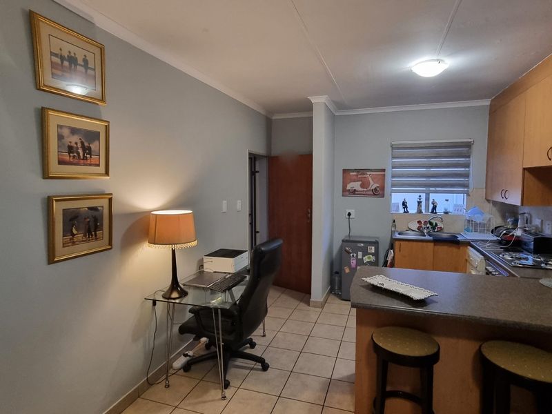 Open-plan living area featuring a functional kitchen with built-in cabinetry, laminate countertops, and tiled flooring, seamlessly connected to a versatile workspace.
