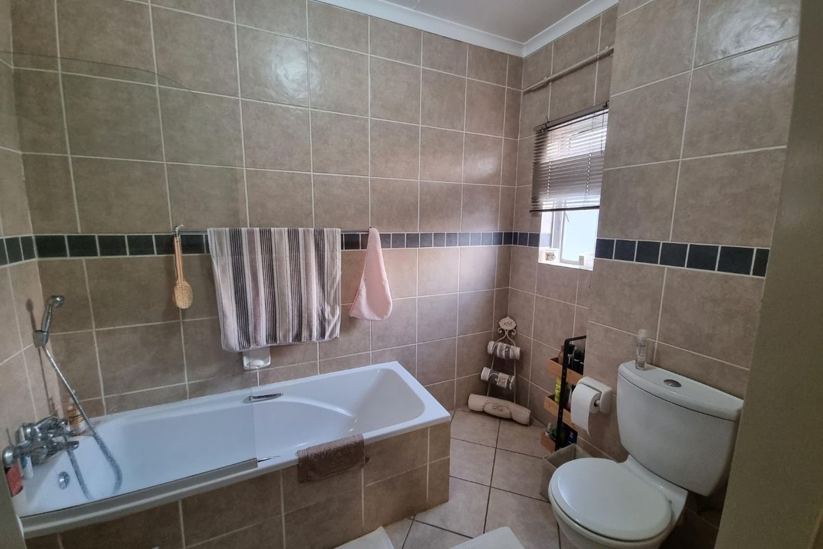 A functional bathroom featuring a built-in bathtub with shower mixer, a standard toilet, and neutral ceramic wall and floor tiling.