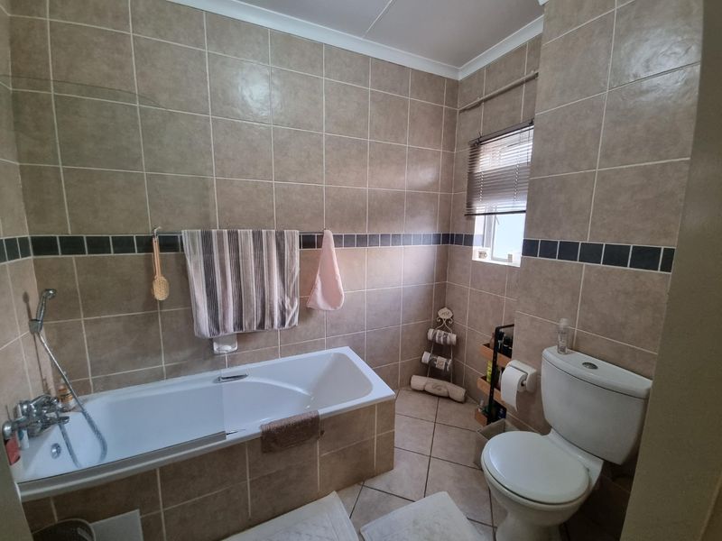 A functional bathroom featuring a built-in bathtub with shower mixer, a standard toilet, and neutral ceramic wall and floor tiling.
