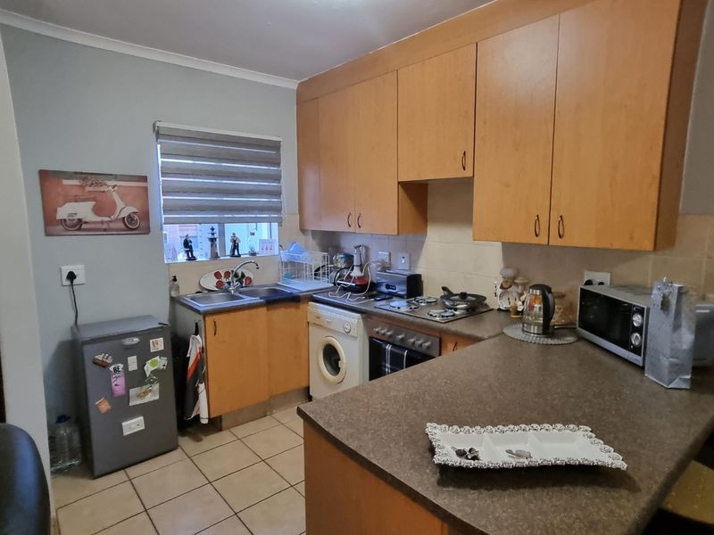 A functional kitchen featuring wooden cabinetry, laminate countertops, a built-in hob and oven, and tiled flooring with a window for natural light.