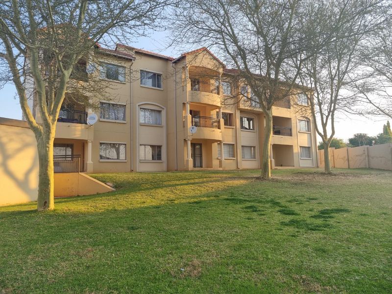 A view of the apartment complex rear facade featuring multiple balconies, plastered exterior walls, and a well-maintained communal garden area.