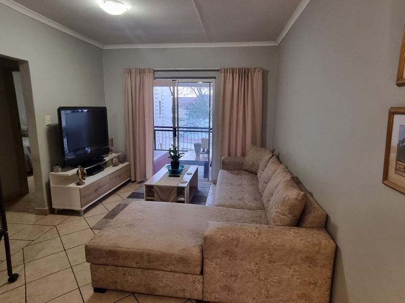 A comfortable living room featuring tiled flooring, cove cornicing, and direct access to a private balcony through sliding glass doors.