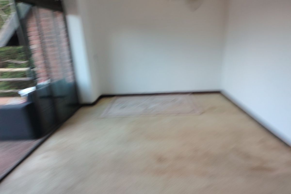 An empty living room featuring carpet flooring, a wall-mounted air conditioning unit, and large sliding glass doors leading to an outdoor area.