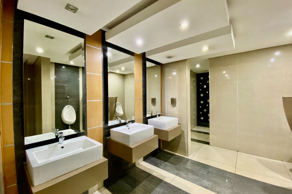 Modern commercial restroom featuring wall-mounted vanity basins, large mirrors, recessed lighting, and high-quality ceramic floor and wall tiling.