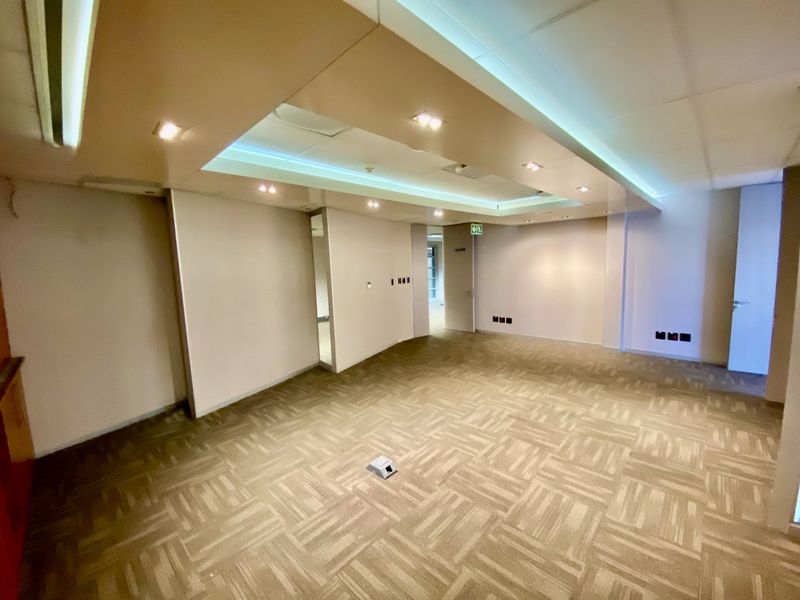A spacious, empty commercial office area featuring recessed ceiling lighting, neutral carpet tiles, and integrated electrical and data connectivity points.