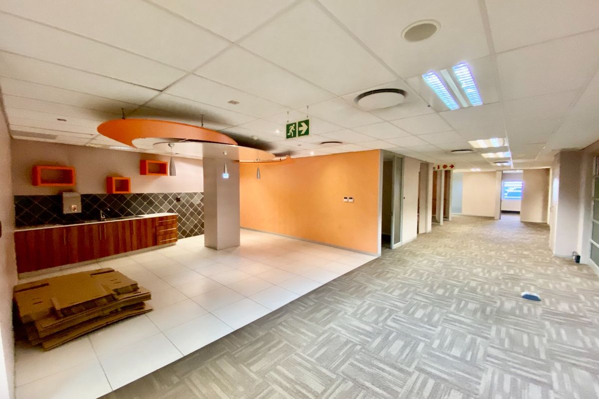 A commercial kitchenette area featuring built-in cabinetry, tiled backsplash, and a drop ceiling, situated within an open-plan office space with carpeted flooring.