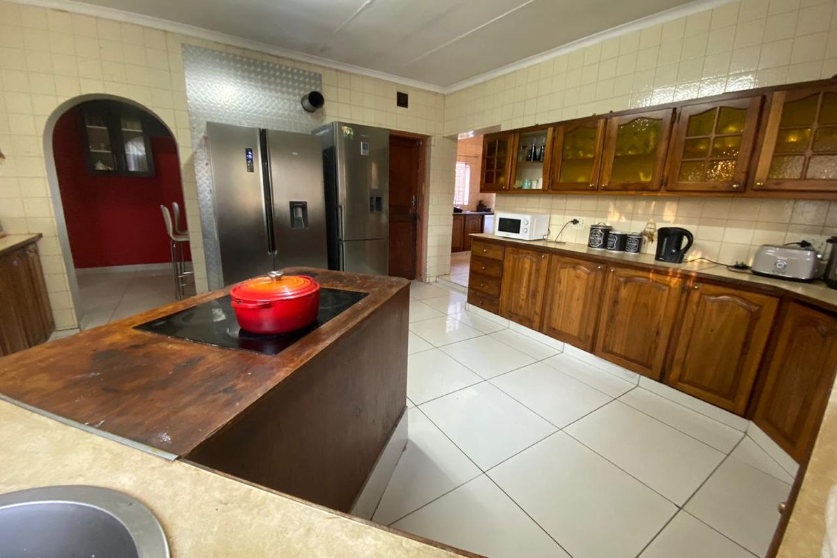 A spacious kitchen featuring wooden cabinetry, tiled flooring, and a central island with a built-in hob, offering a functional layout with classic finishes.