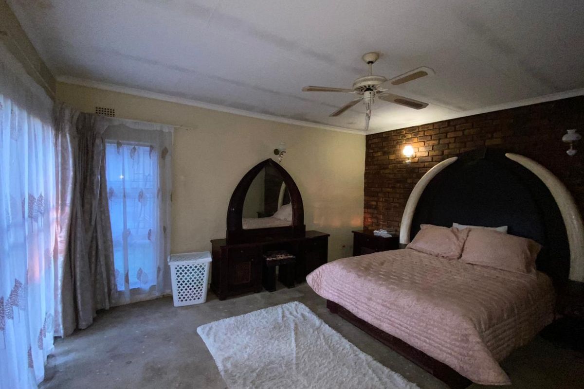 A bedroom featuring an exposed brick accent wall, ceiling fan, and wall sconce lighting, requiring cosmetic updates to the ceiling and flooring.