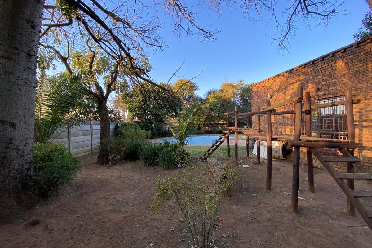 A spacious rear garden featuring a swimming pool, mature trees, and a brick exterior wall, offering potential for landscaping and outdoor entertainment development.