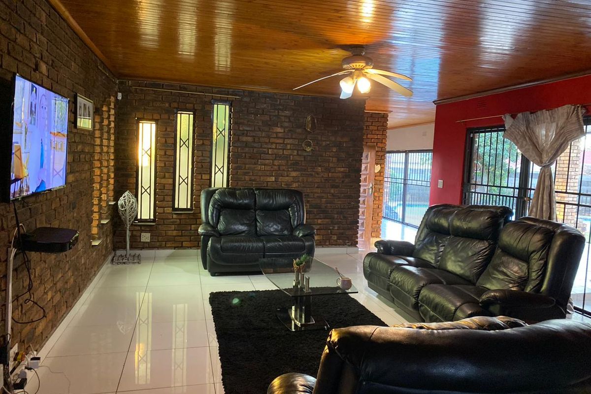 Spacious living room featuring exposed brick walls, a warm timber ceiling, and polished floor tiles, offering a distinct character and direct access to the outdoors.