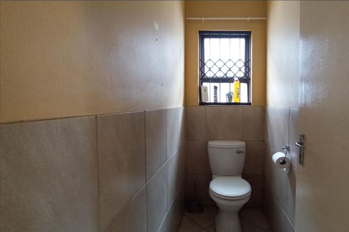 A compact guest bathroom featuring tiled walls, a standard toilet, and a window with a security gate.